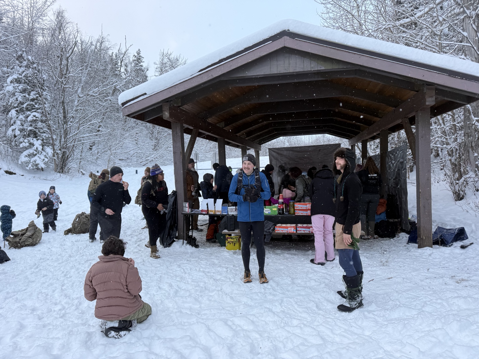 Participants and families gathering at a snowy Toughest Alive basecamp shelter.