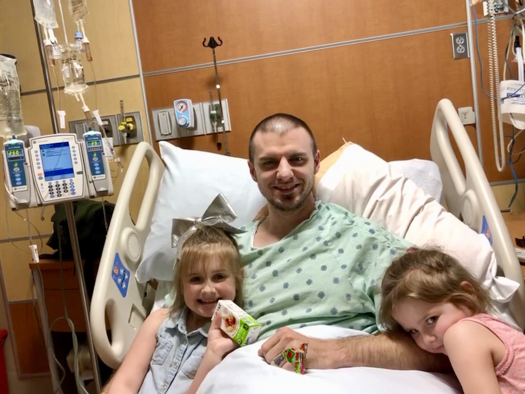 Andrew smiling from a hospital bed with two children beside him.